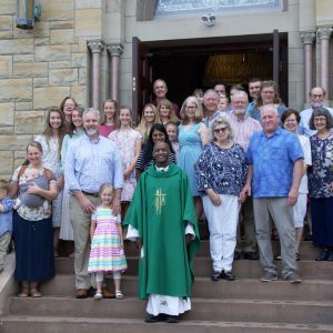 People stand on the steps of a church with a Priest.
