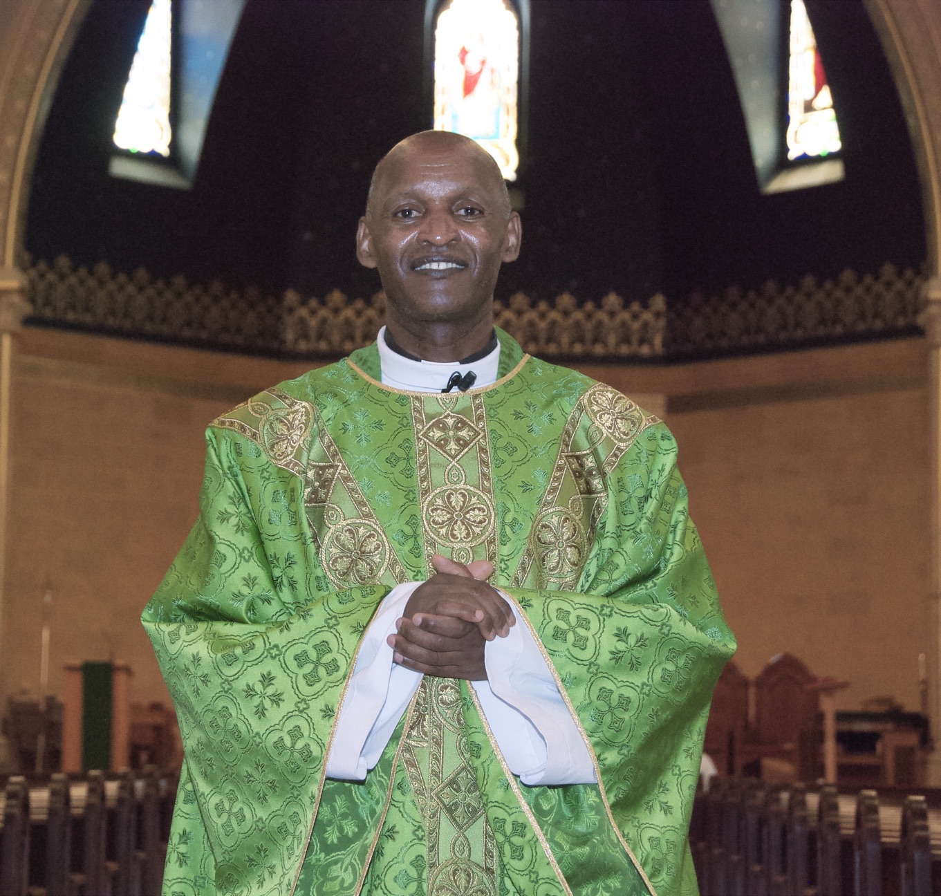 A vested Priest stands inside a church.